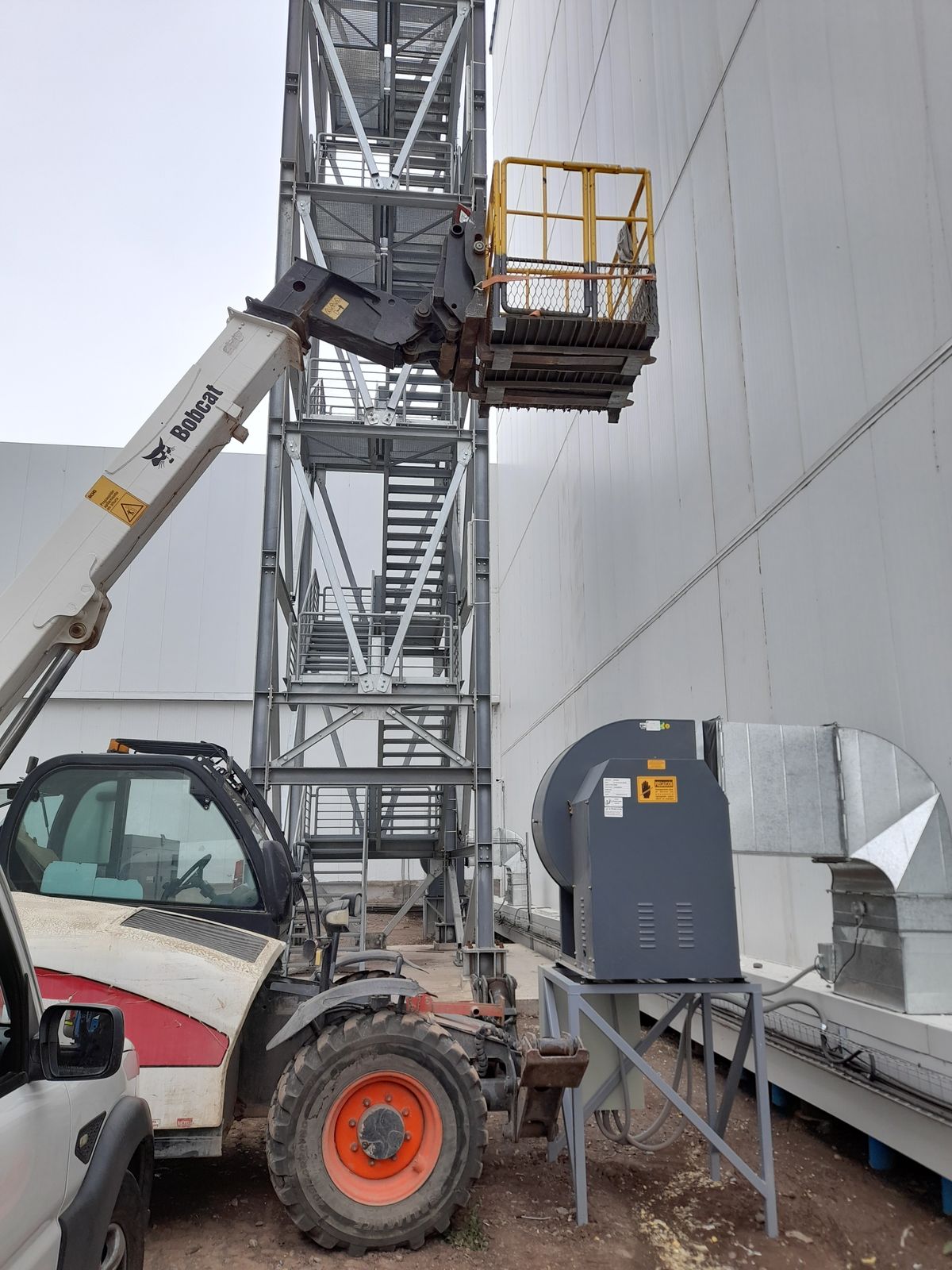 Manipulador telescópico con canastillo junto a una torre de escalera